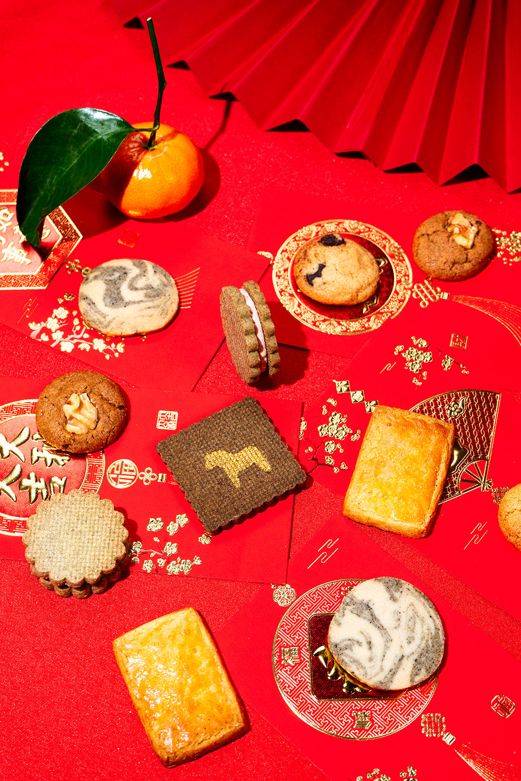 Assorted cookies on a red decorative surface with a fan in the background